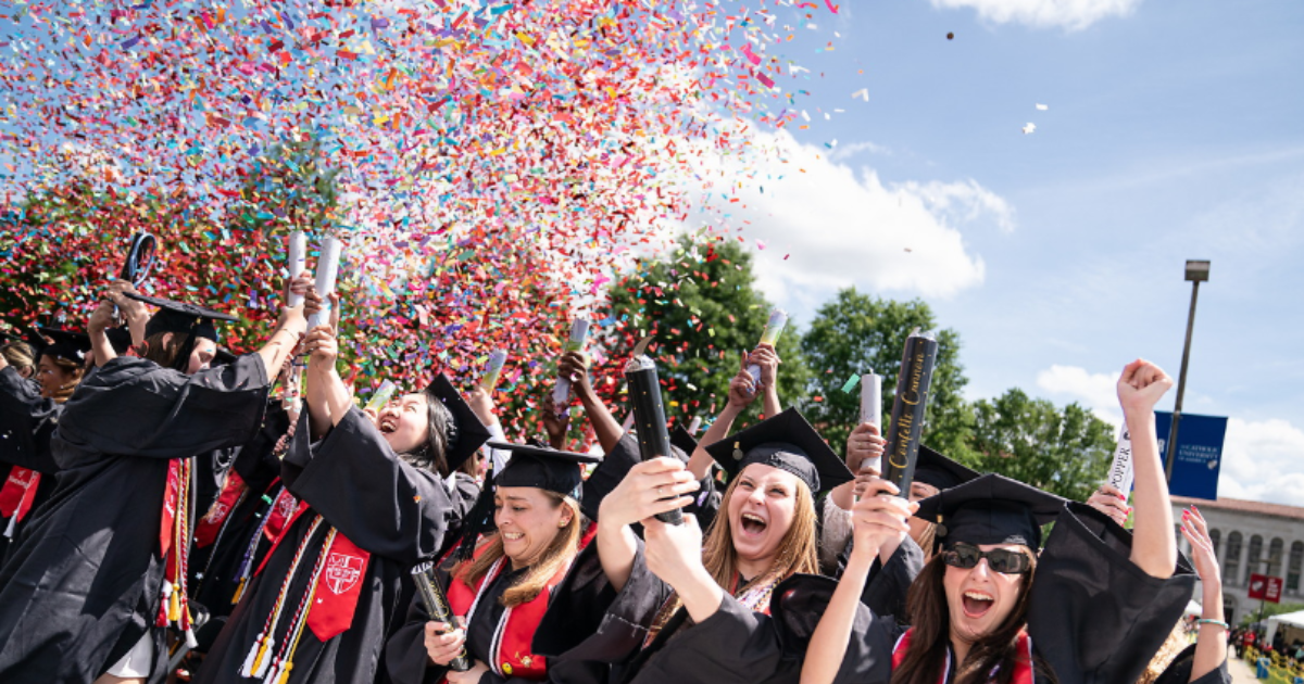 A group of people in black graduations robes smiling with confetti in the background